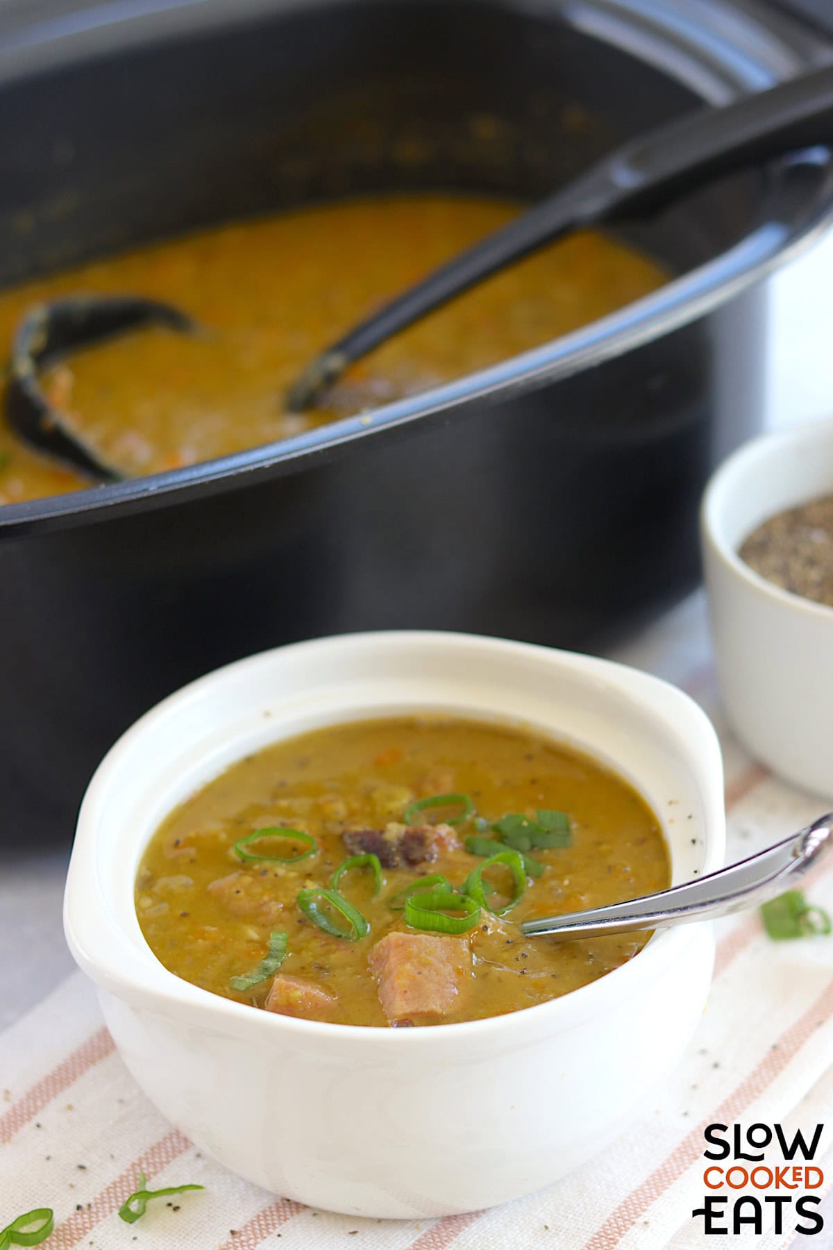 Crockpot split pea and ham soup recipe served in a white round bowl and silver spoon.