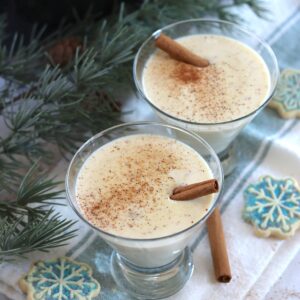 Crockpot eggnog served in a glass with cinnamon dusted on top and a cinnamon stick.