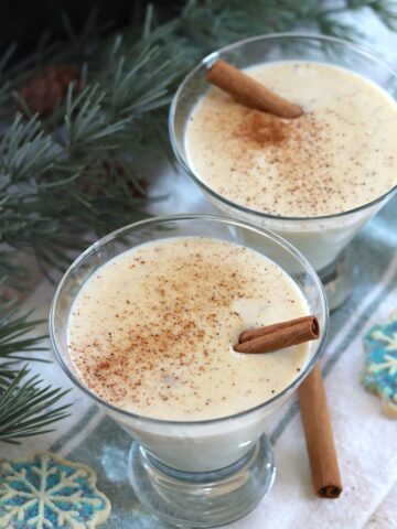 Crockpot eggnog served in a glass with cinnamon dusted on top and a cinnamon stick.