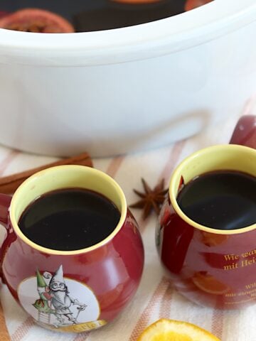 Two Red and yellow mugs filled with mulled wine recipe crockpot.