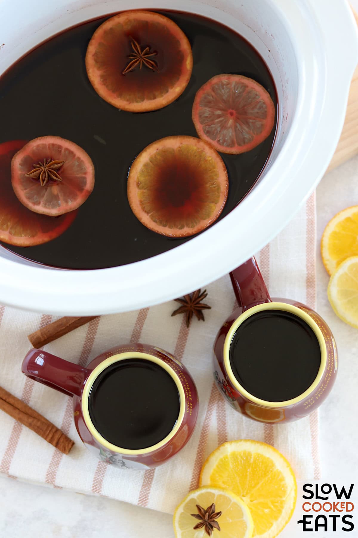A white round slow cooker ad two mugs filled with mulled wine recipe crockpot.