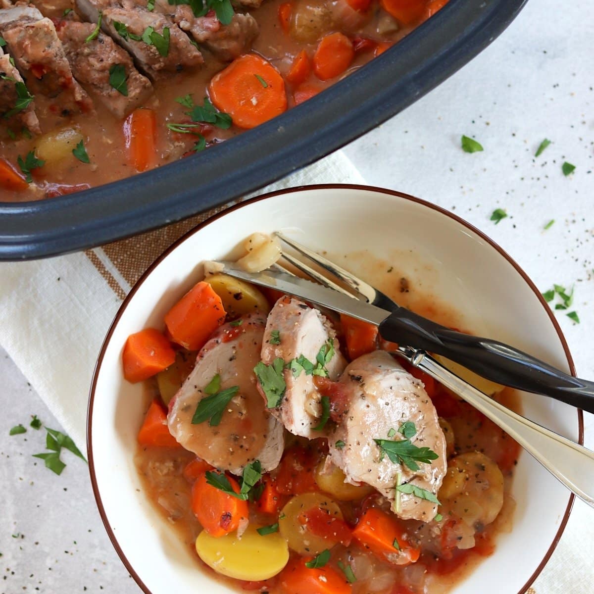 Ranch crockpot pork tenderloin with vegetables in a white bowl with silver fork and knife.