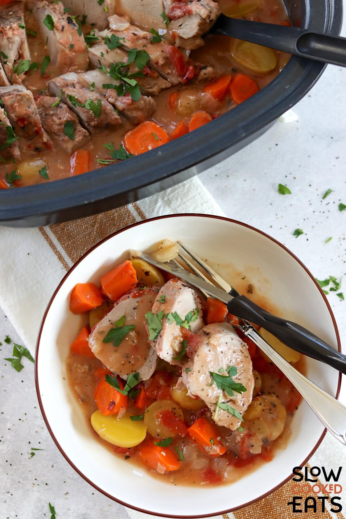 Ranch crockpot pork tenderloin with vegetables served in a white bowl with silver fork and knife.