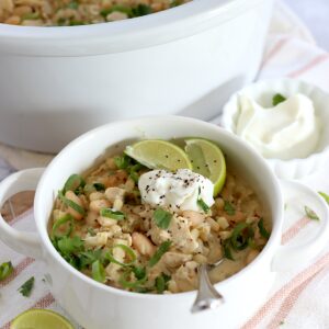 A small white crock filled with leftover slow cooker turkey white chili and silver spoon.