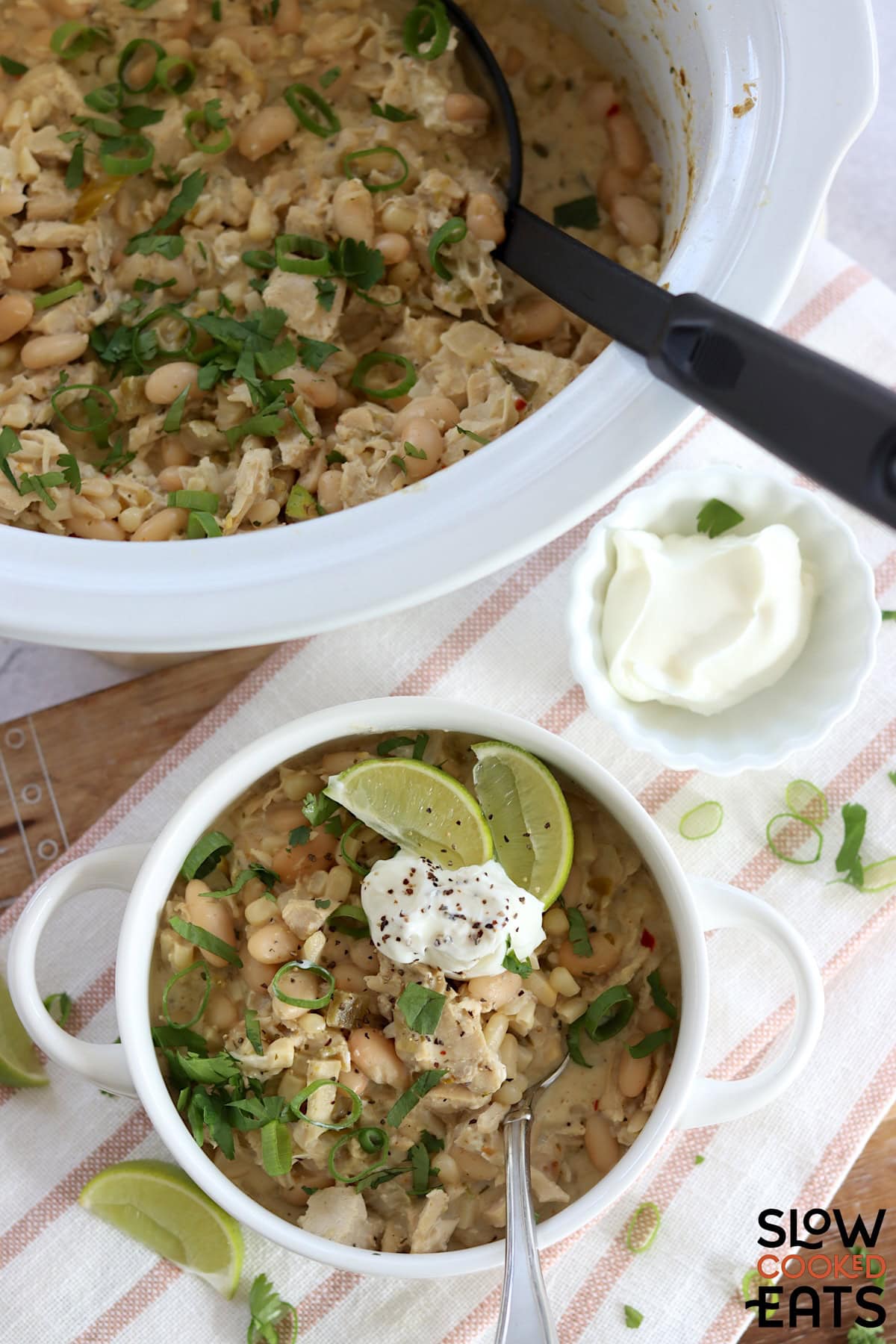 A small white crock filled with leftover slow cooker turkey white chili and silver spoon.