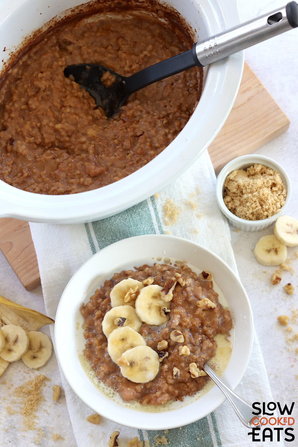 Crockpot banana oatmeal served in a white round bowl and silver spoon, next to a white round slow cooker filled with the overnight oatmeal.