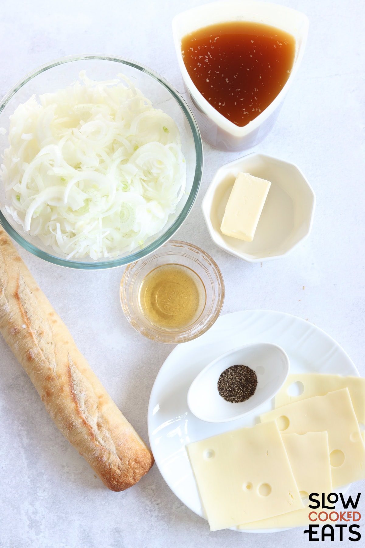 Ingredients needed to make crockpot French onion soup on a white marble countertop.
