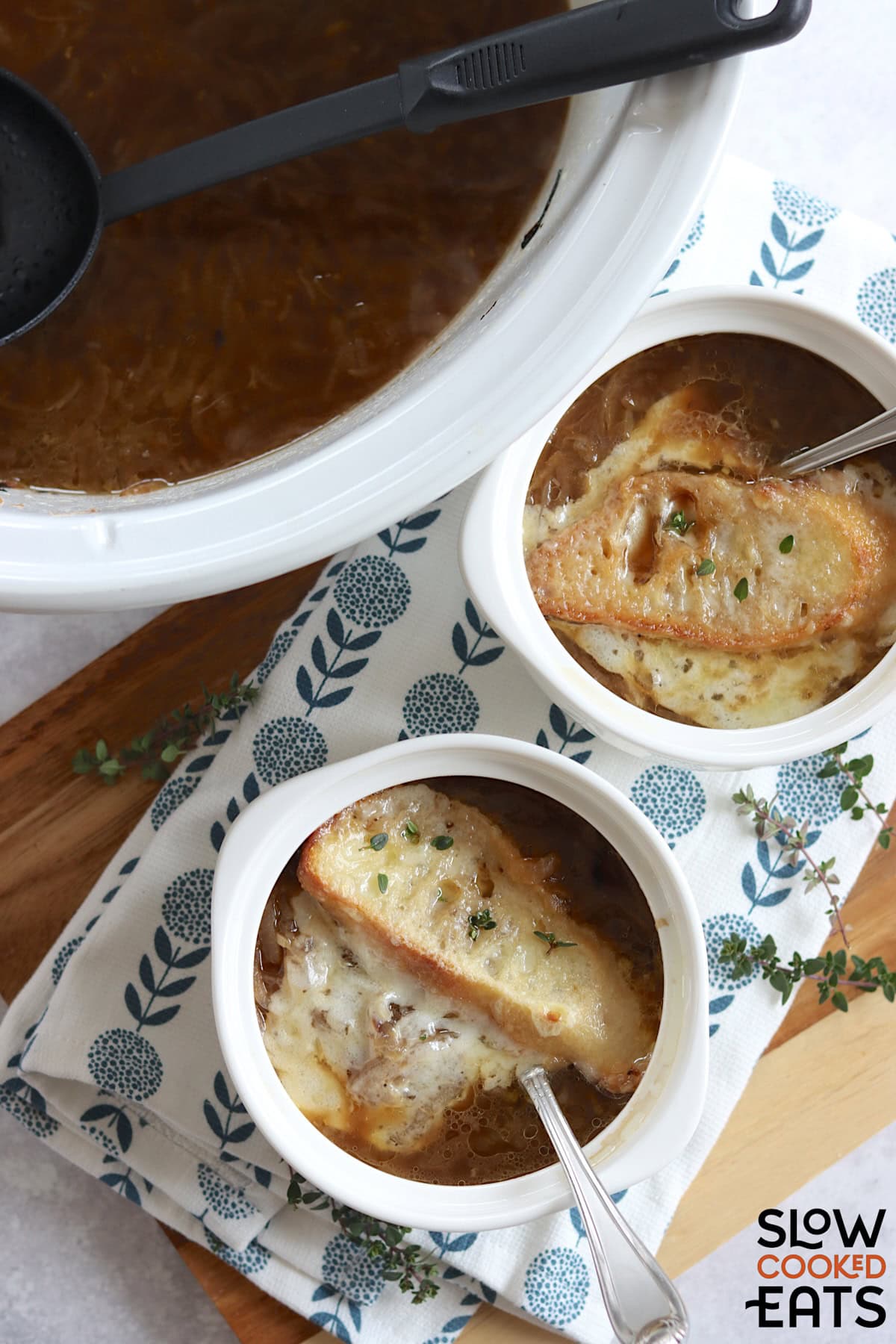 Crockpot French onion soup served in small round white crocks and silver spoons.