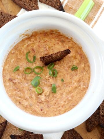 Crockpot Reuben dip recipe in a white round small slow cooker garnished with sliced green onion.