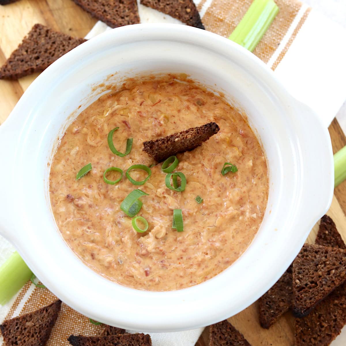 Crockpot Reuben dip recipe in a white round small slow cooker garnished with sliced green onion.
