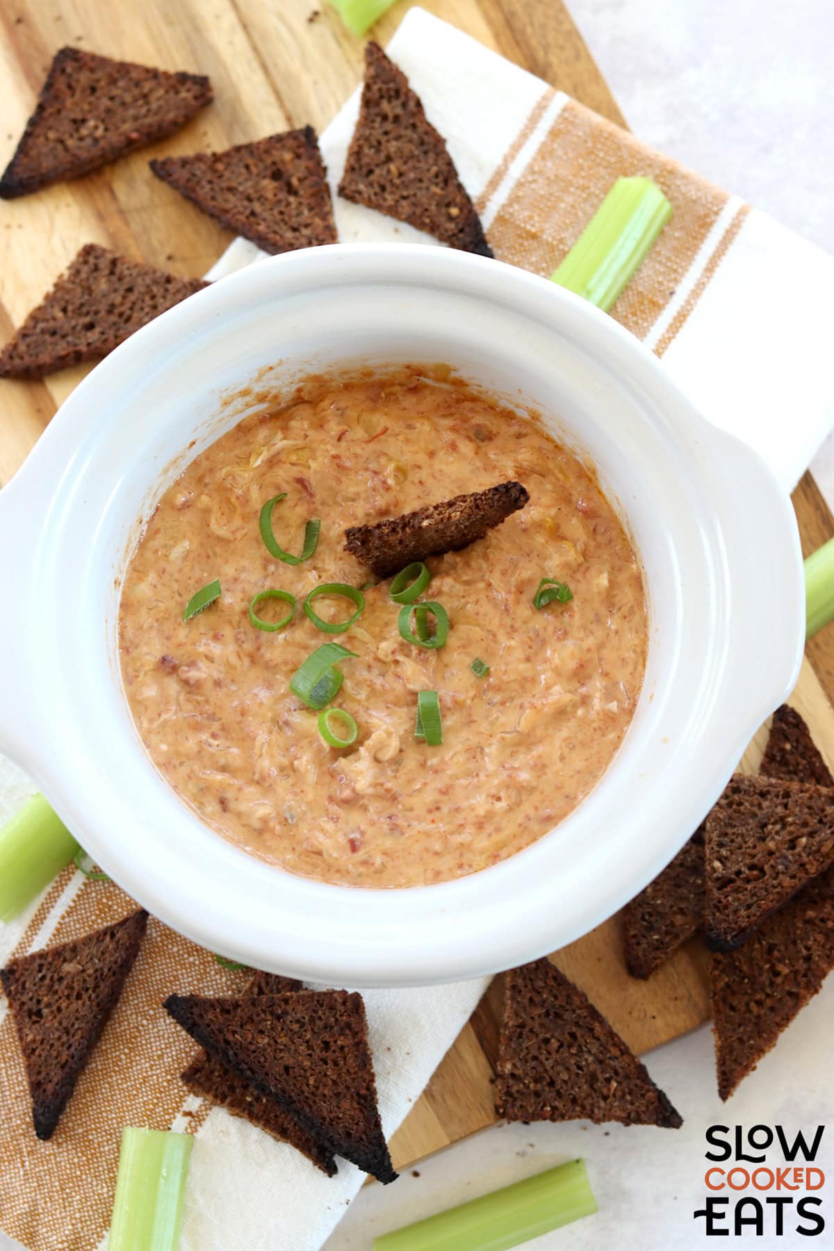 Crockpot Reuben dip recipe in a white round slow cooker, topped with sliced green onion.