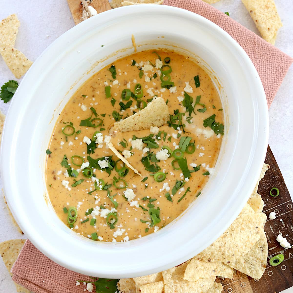 Slow cooker queso Blanco dip in a white oval crockpot and garnished with green onion and extra cheese.