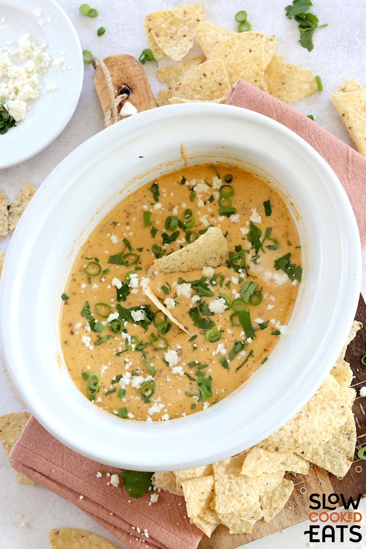 Slow cooker queso blanco dip in a white round crockpot garnished with sliced green onion and extra cheese.