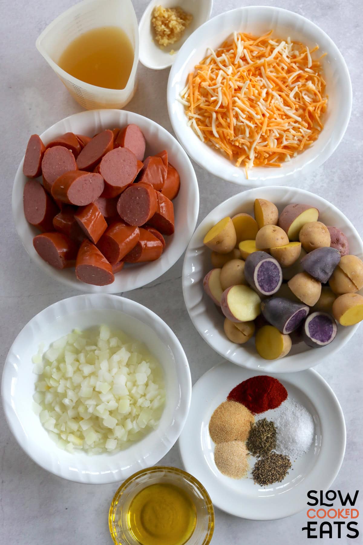 Ingredients needed to make crockpot sausage and potatoes on a white marble countertop.