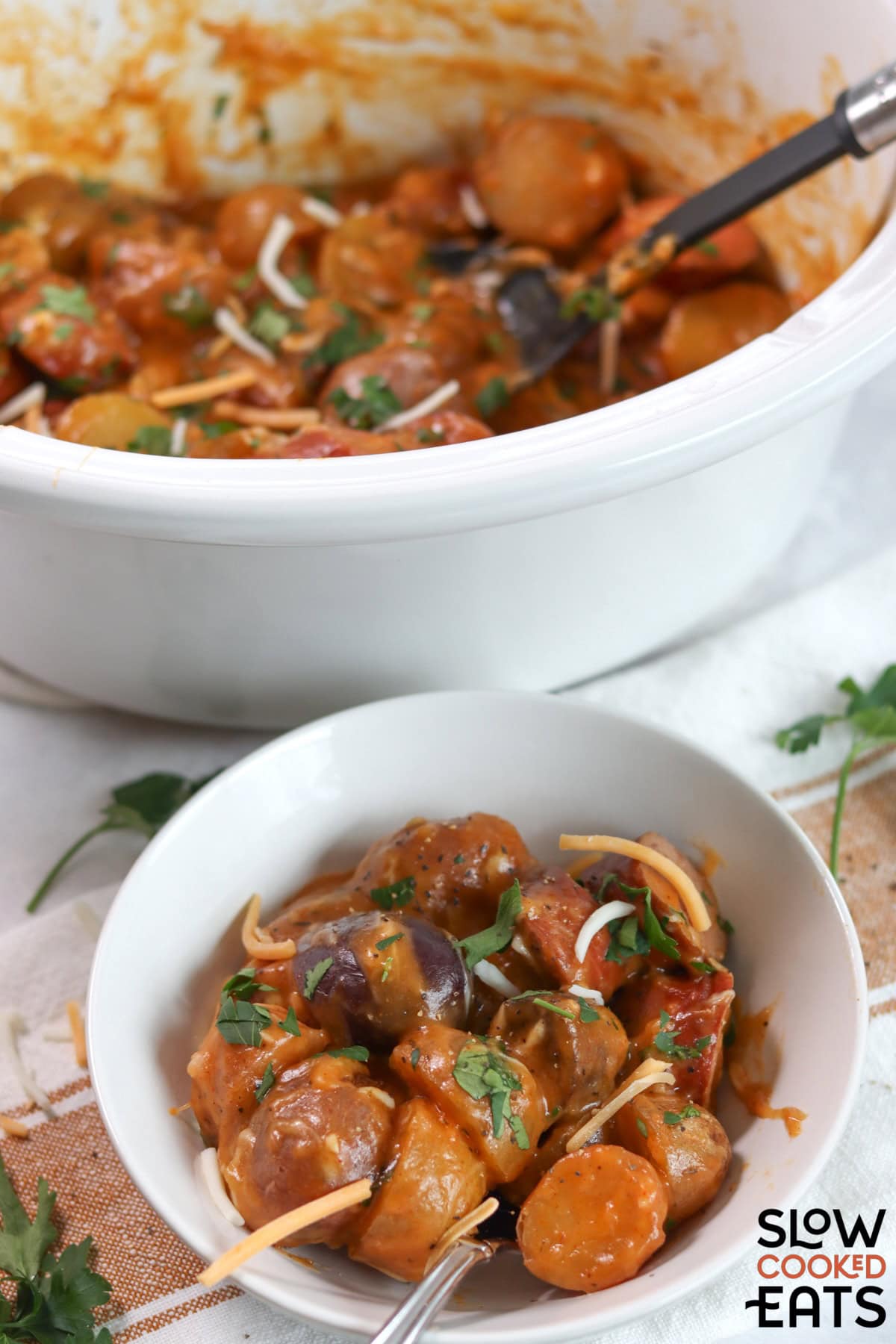 Crockpot sausage and potatoes served in a white round bowl and silver spoon.
