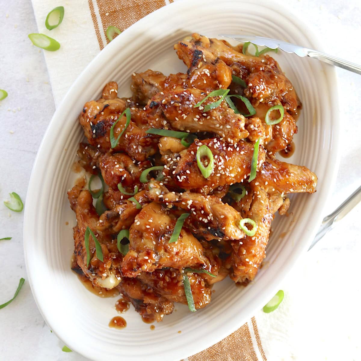Crockpot teriyaki chicken wings on a white oval plate and garnished with sliced green onion and sesame seeds.