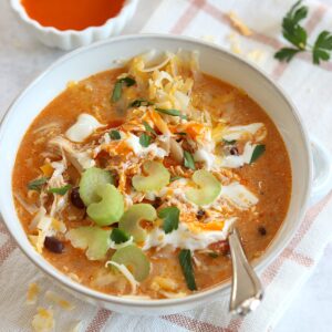 The best buffalo chicken chili crockpot recipe served in a white round bowl and silver spoon.