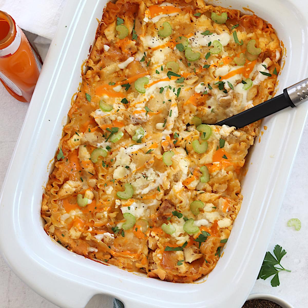 Buffalo chicken lasagna crockpot recipe served in white serving dish and black spoon.