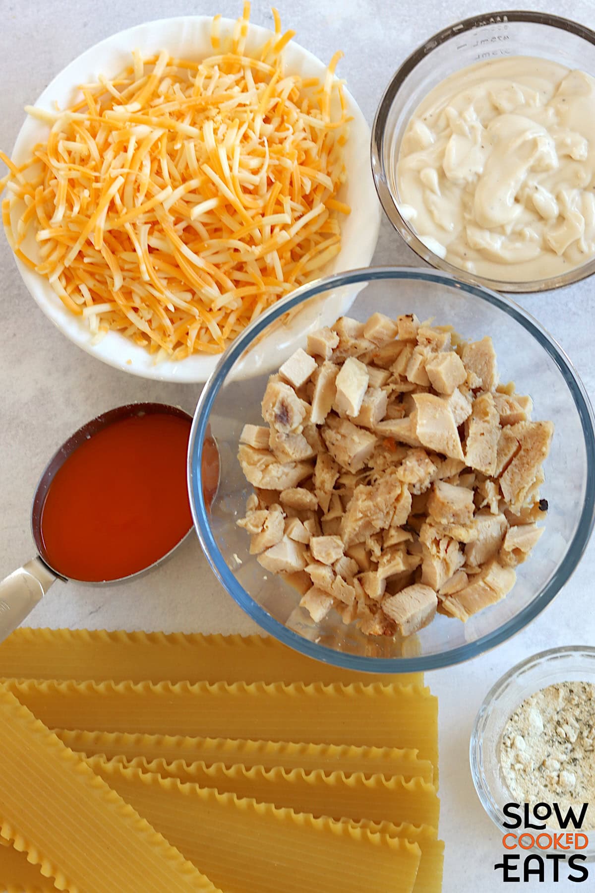 Buffalo chicken lasagna crockpot recipe ingredients on a white marble countertop.