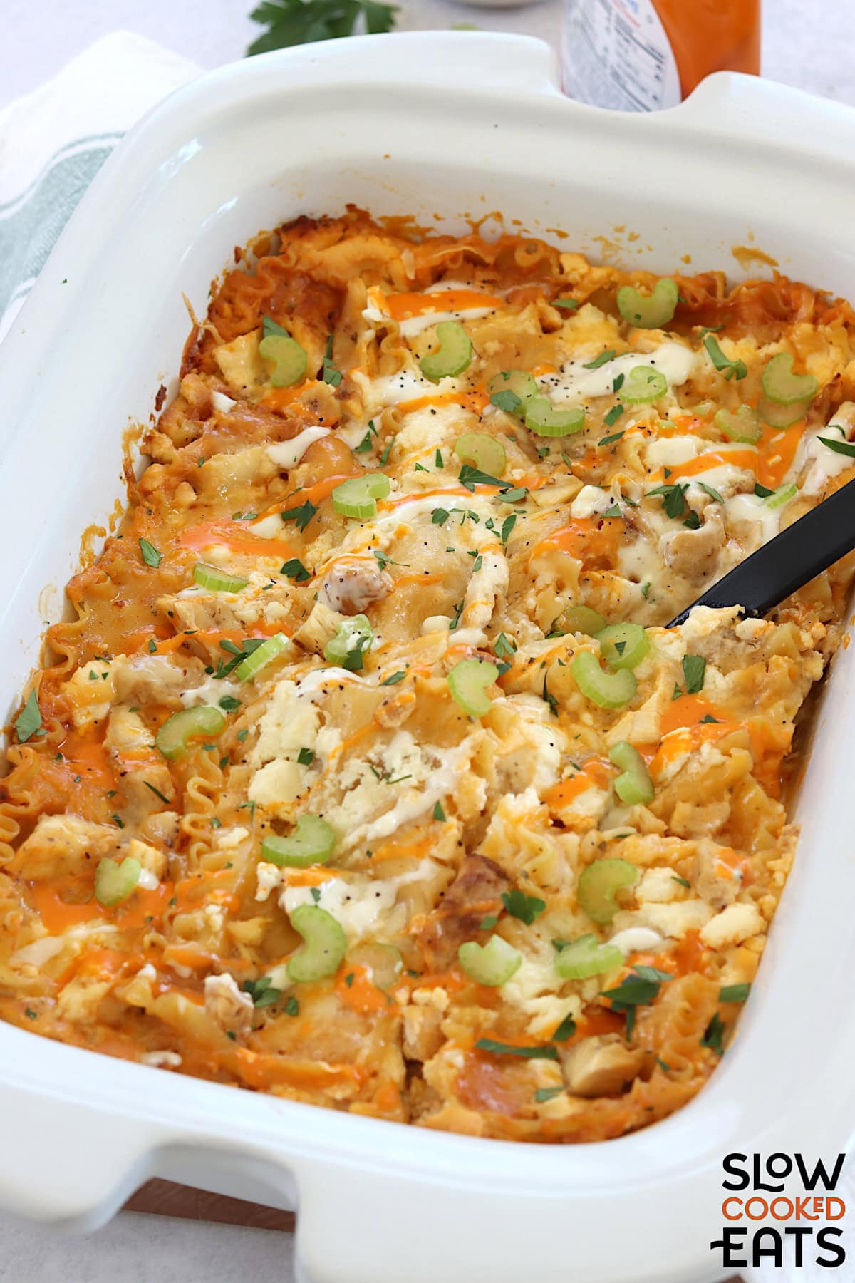 Buffalo chicken lasagna crockpot recipe baked in a white rectangle dish with a black serving spoon.