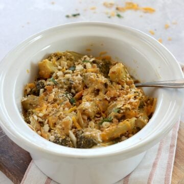 Crockpot broccoli cheese casserole in an oval white slow cooker and a silver serving spoon.