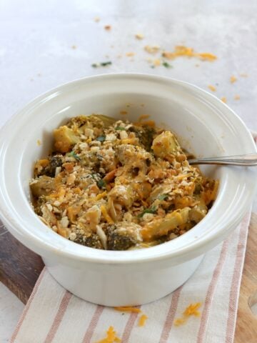 Crockpot broccoli cheese casserole in an oval white slow cooker and a silver serving spoon.