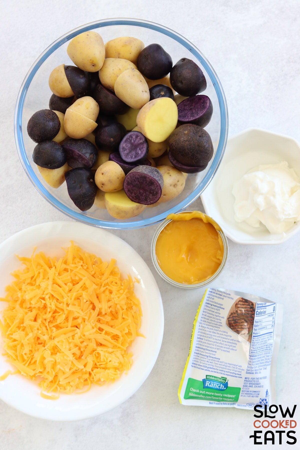 Ingredients needed to make crockpot cheesy potatoes on a white marble countertop.