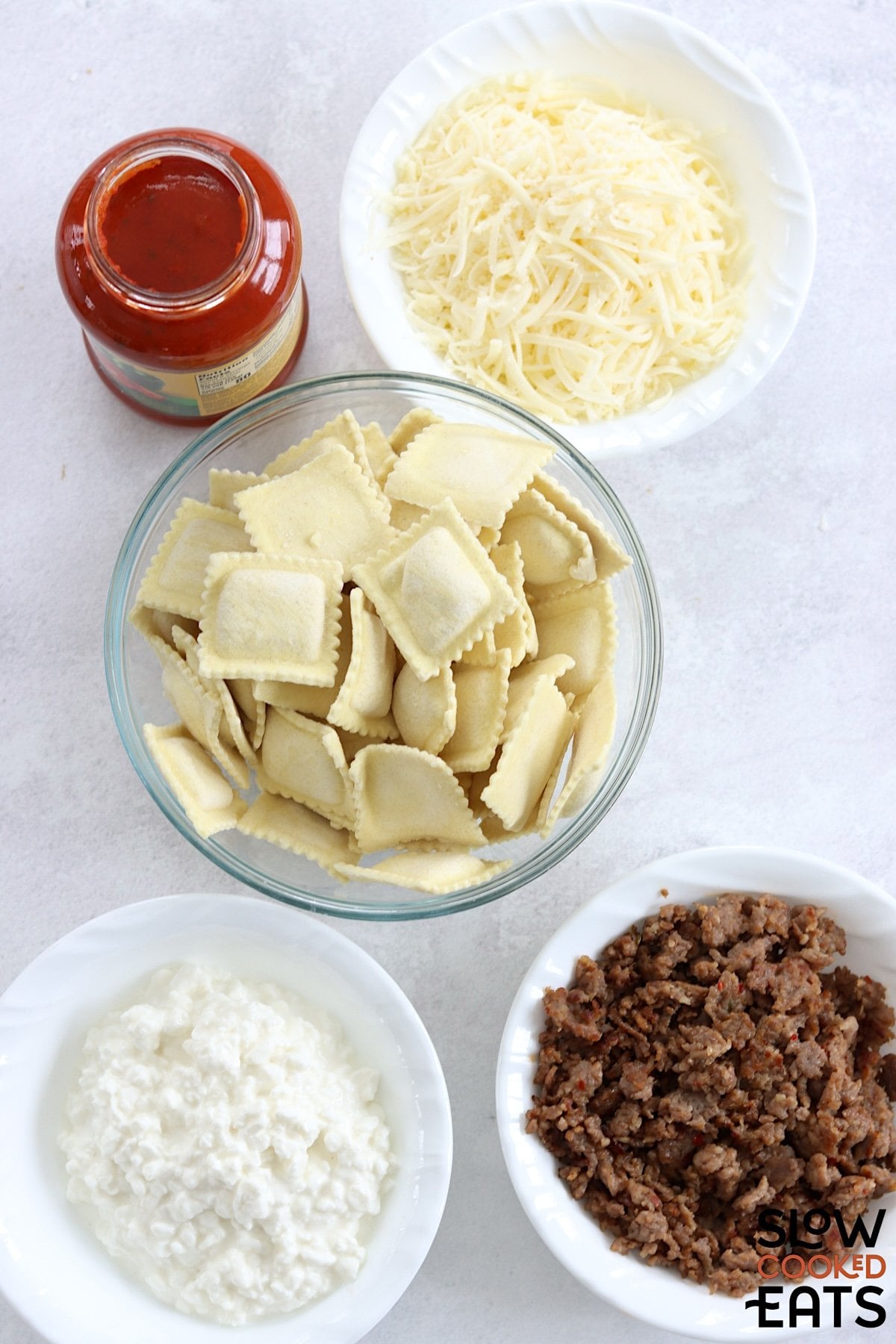 Ingredients needed to make crockpot ravioli lasagna on a white marble countertop.