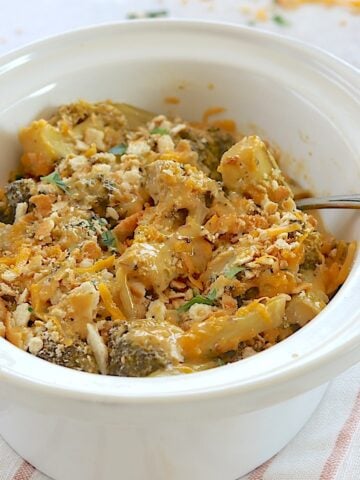 Crockpot broccoli cheese casserole in an oval white slow cooker and a silver serving spoon.