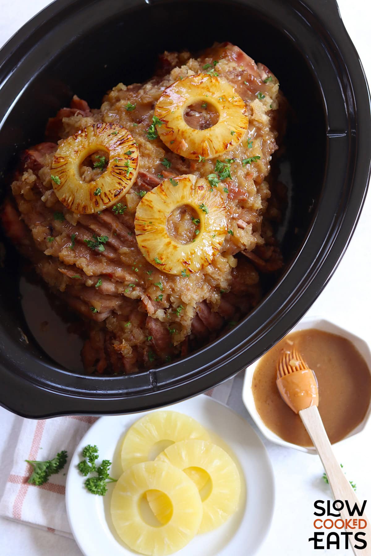 A black oval slow cooker filled with pineapple crockpot ham and topped with seared pineapple slices.