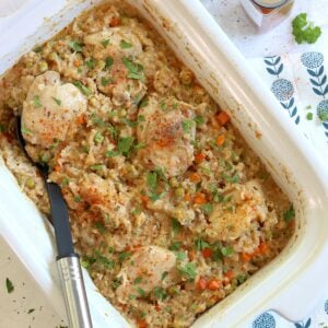Crock pot chicken thighs and rice in a white rectangular slow cooker and a black serving spoon.
