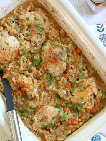 Crock pot chicken thighs and rice in a white rectangular slow cooker and a black serving spoon.