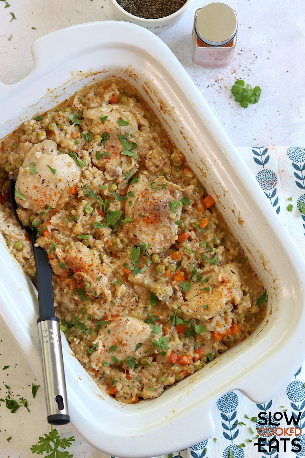Crock pot chicken thighs and rice in a white rectangle slow cooker and a black serving spoon.
