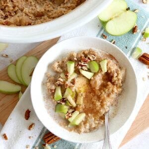 Apple cinnamon crockpot oatmeal recipe in a round white bowl and silver spoon, garnished with diced green apple and chopped pecans.