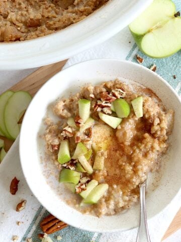 Apple cinnamon crockpot oatmeal recipe in a round white bowl and silver spoon, garnished with diced green apple and chopped pecans.