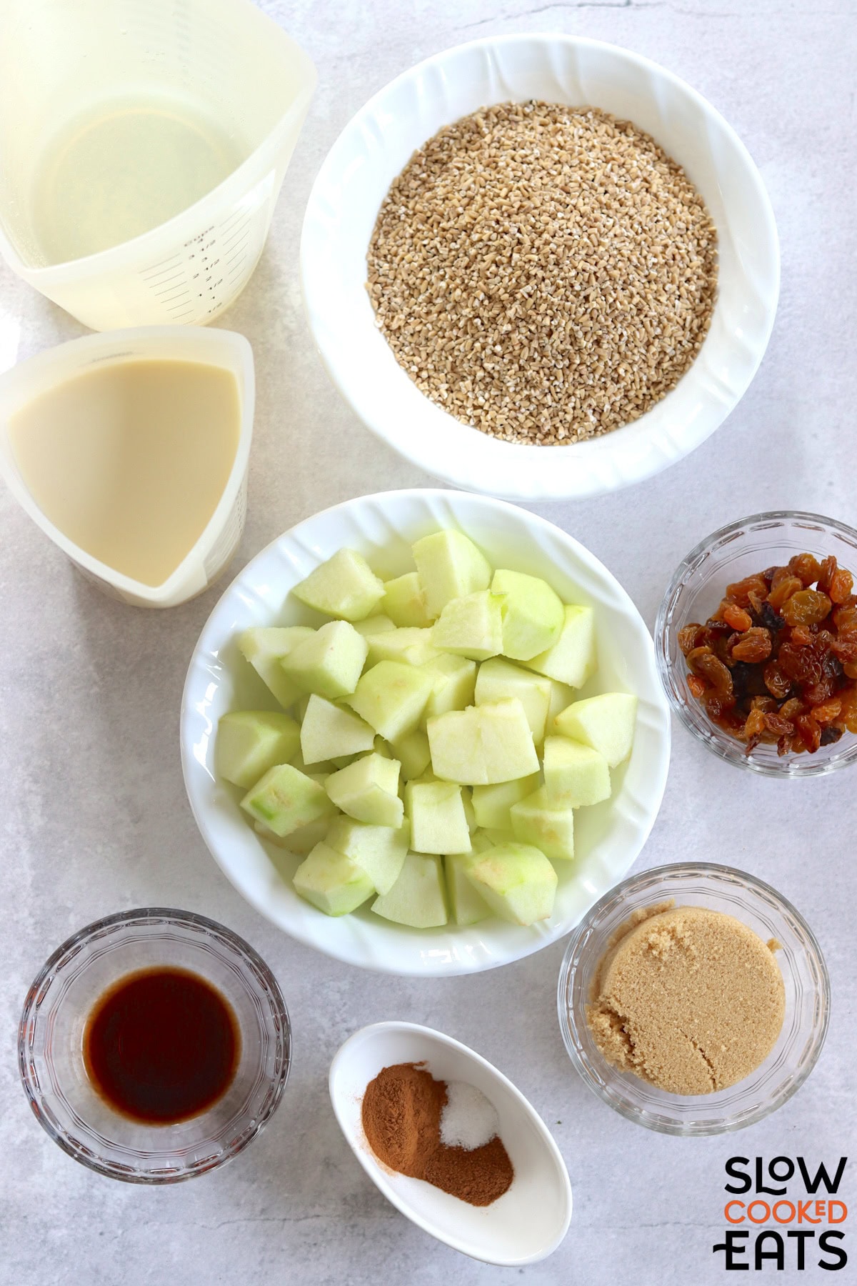 Ingredients needed to make apple cinnamon crockpot oatmeal recipe on a white marble countertop.