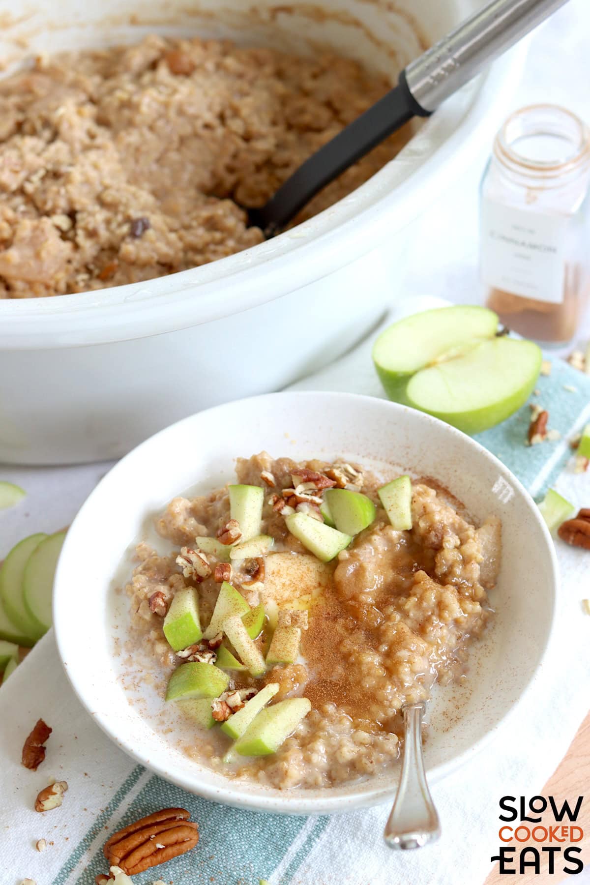 Apple cinnamon crockpot oatmeal recipe in a round white bowl garnished with diced green apple and chopped pecans.