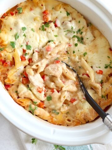 Crockpot Cajun chicken alfredo in a white oval slow cooker and a black serving spoon.