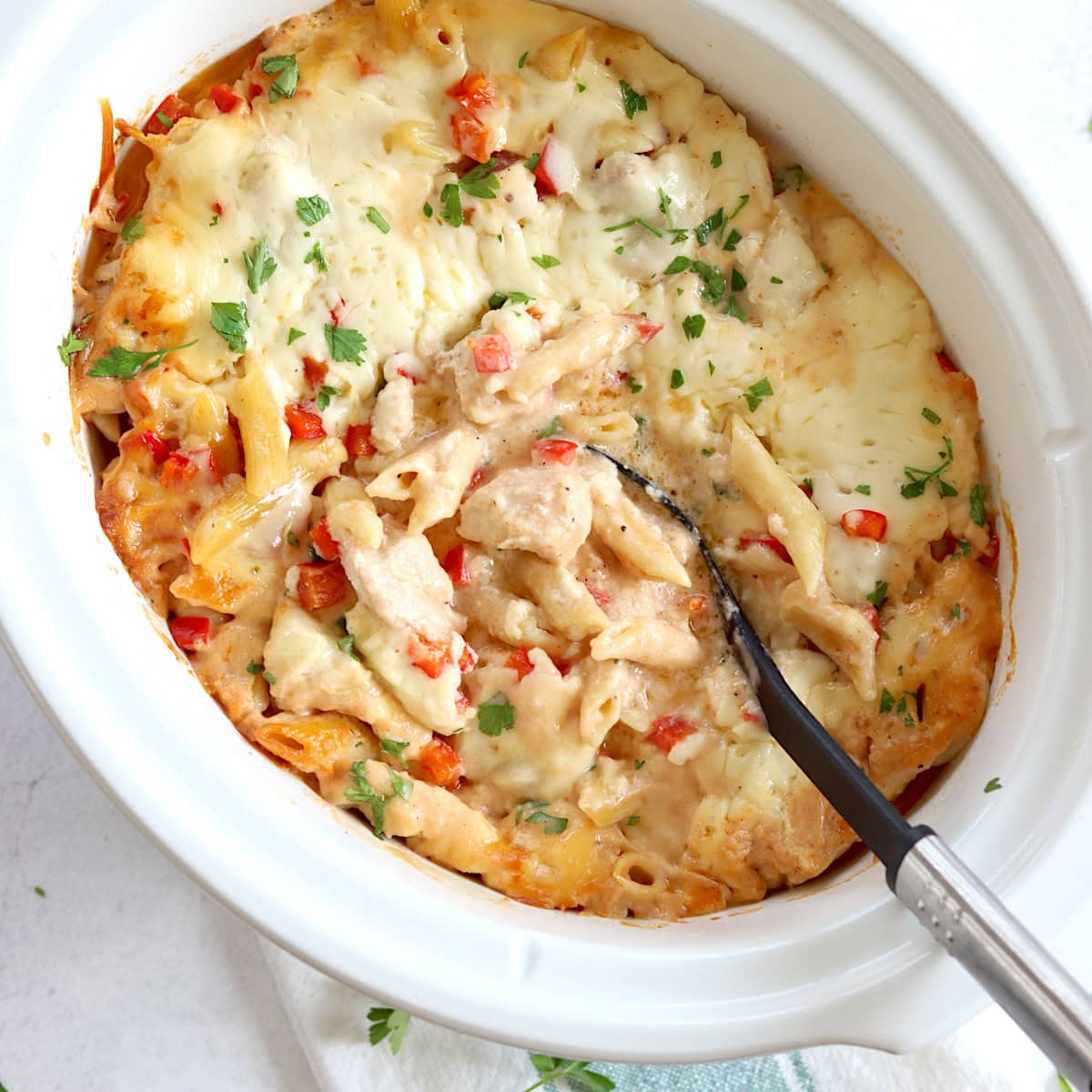 Crockpot Cajun chicken alfredo in a white oval slow cooker and a black serving spoon.