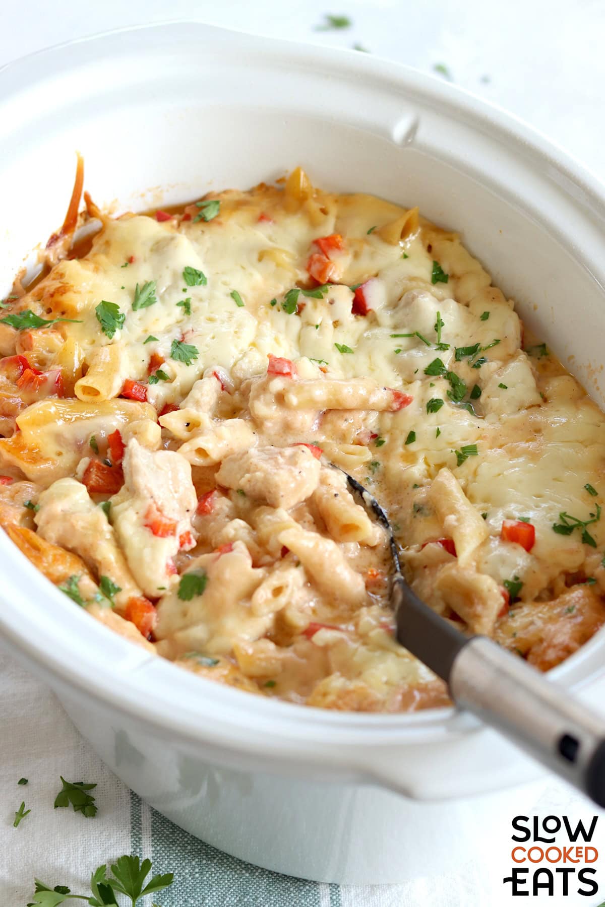 Crockpot Cajun chicken alfredo in a white oval slow cooker and a black serving spoon.