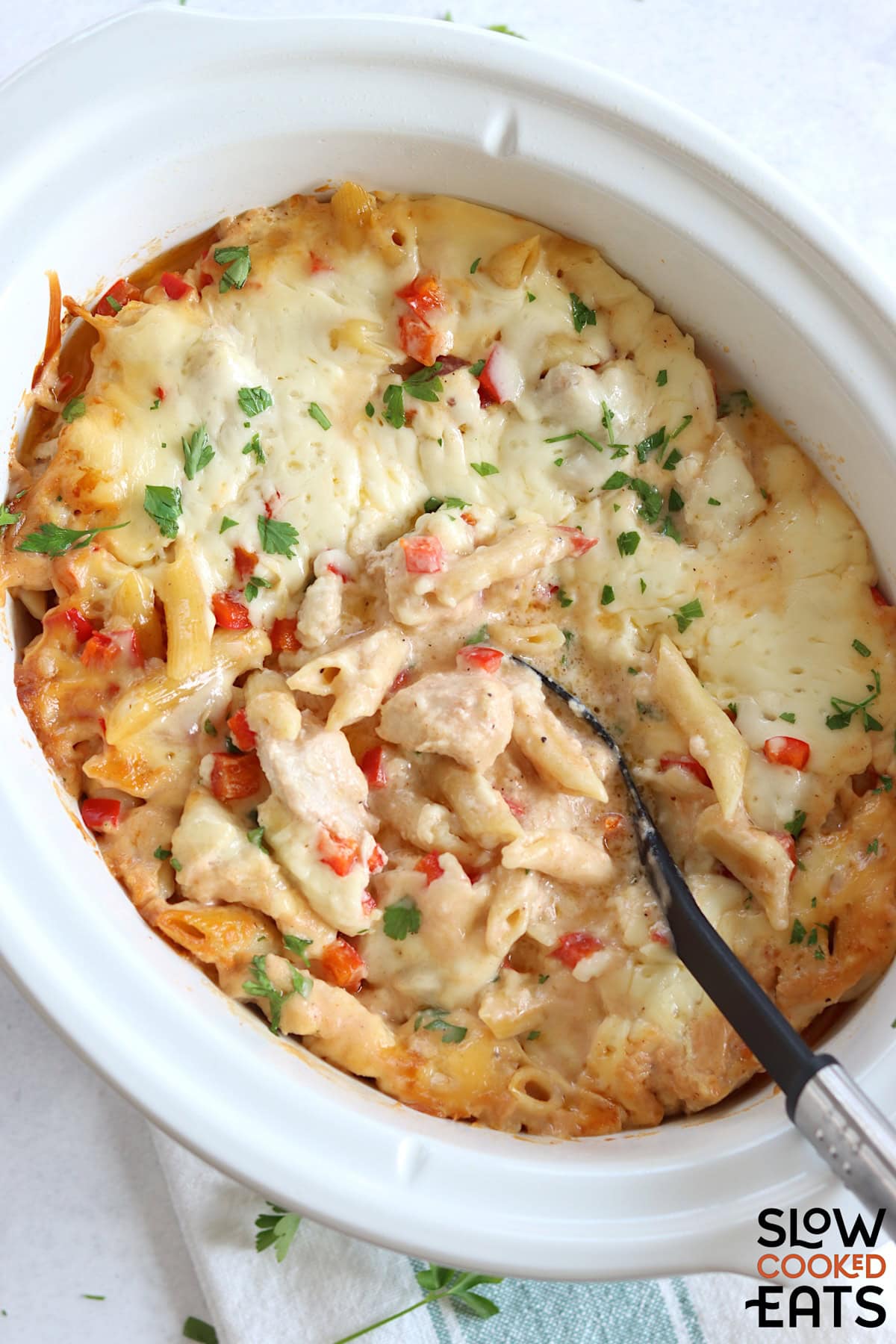 Crockpot Cajun chicken alfredo in a white oval slow cooker and a black serving spoon.