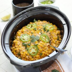 Mexican street corn crockpot recipe served in a black oval slow cooker and garnished with slices of jalapeno on top.