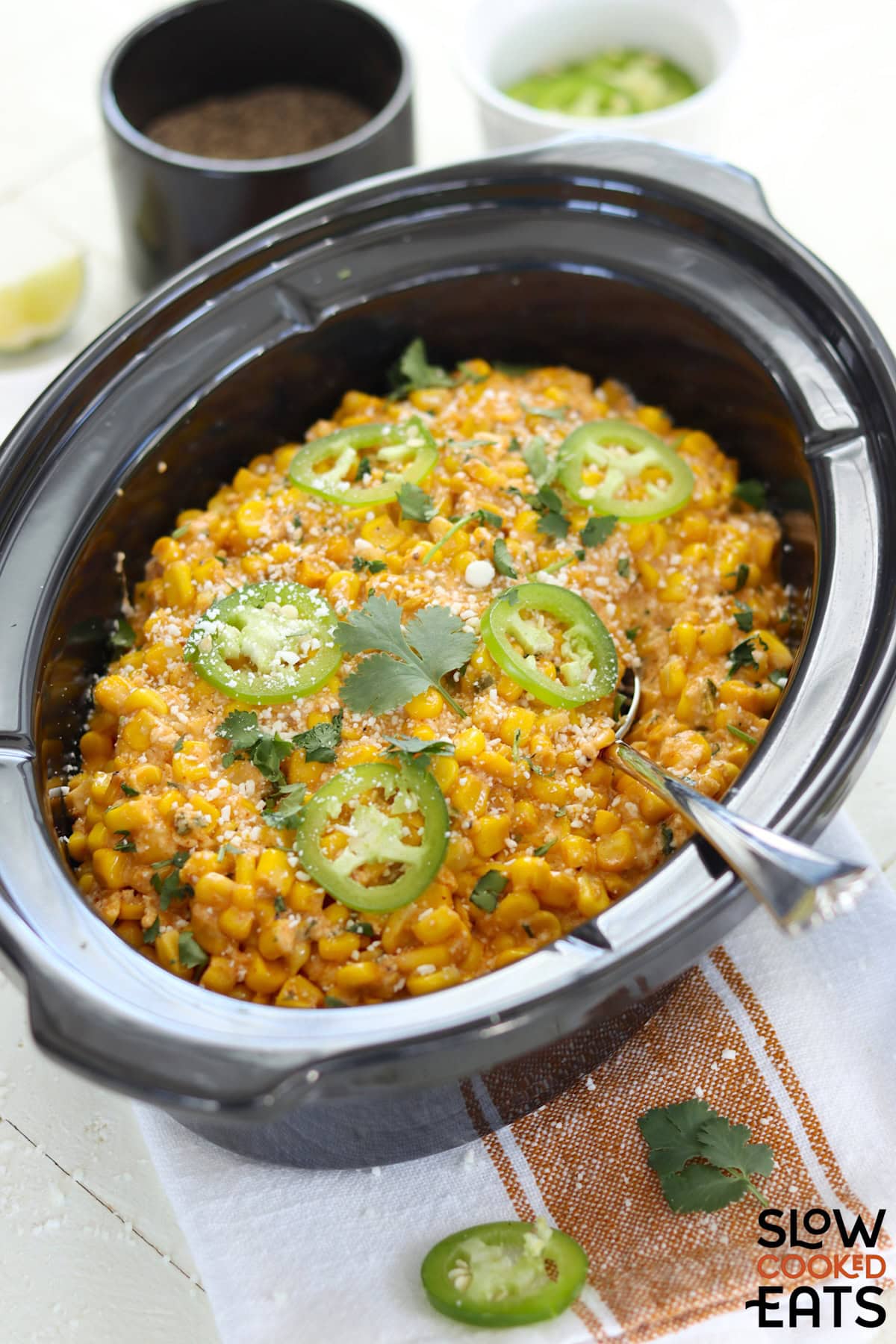 Mexican street corn crockpot recipe served in a black slow cooker and garnished with jalapeno slices on top.