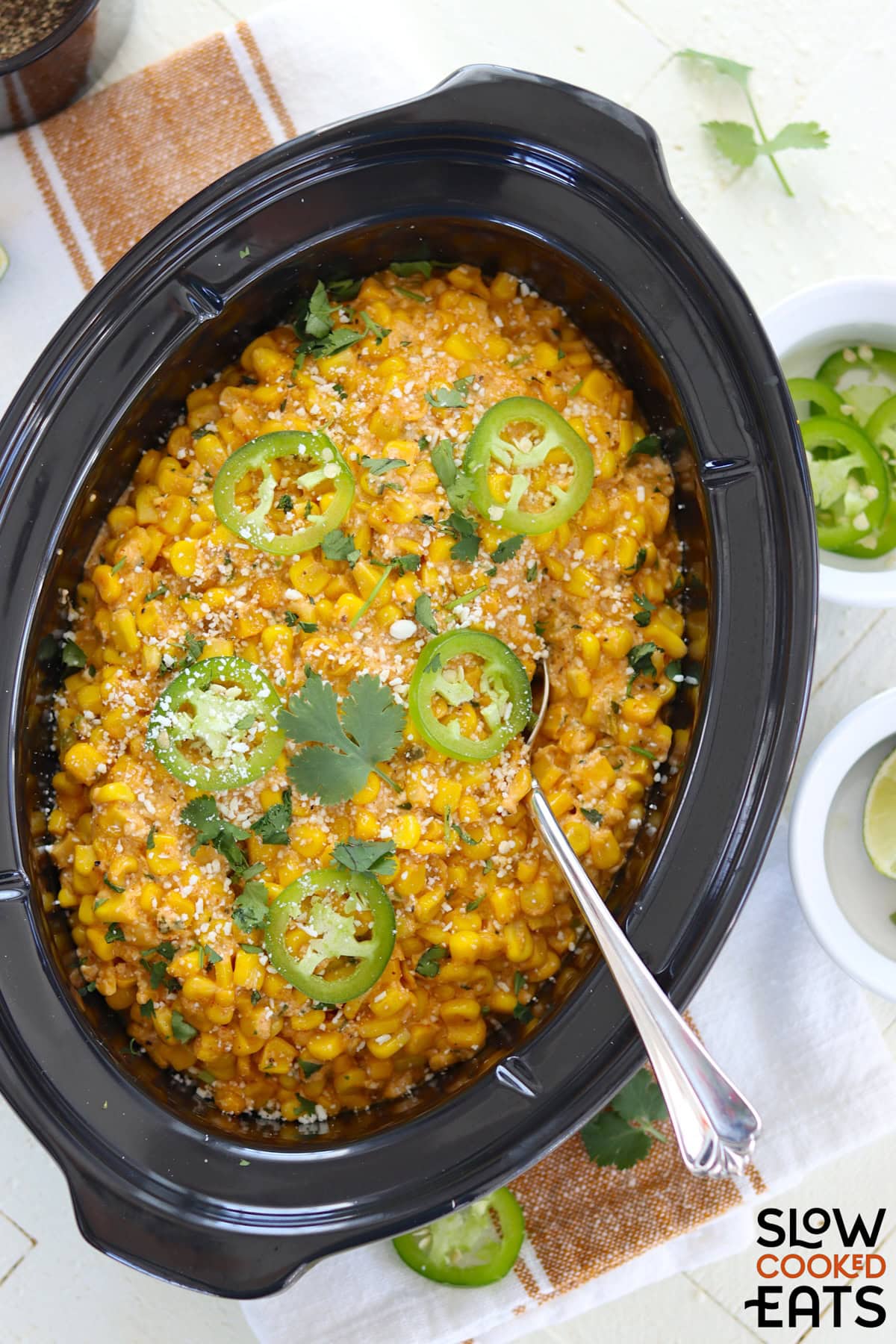 Mexican street corn crockpot recipe served in a black oval slow cooker and garnished with jalapeno slices on top.