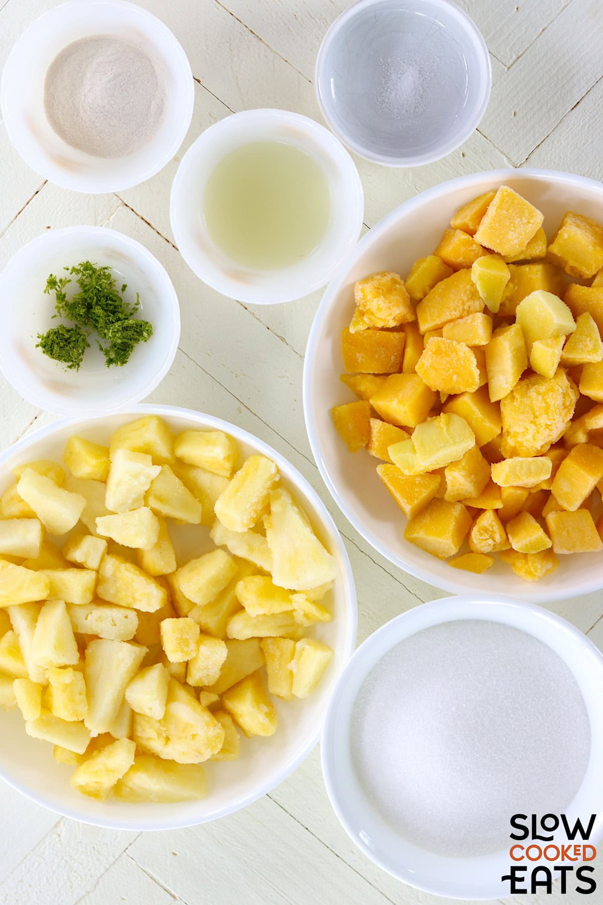 Ingredients needed for making mango pineapple crockpot jam on a white wooded board.