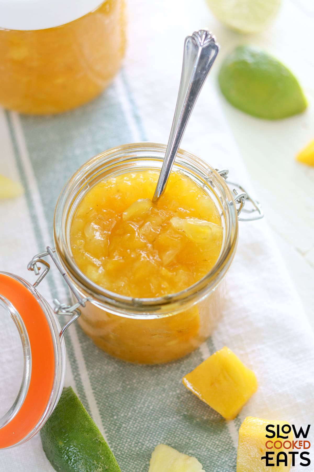 A lidded jar of pineapple mango lime crockpot jam in a lidded glass jar with a spoon.