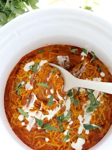 Slow cooker refried beans in a round white crockpot and a white serving spoon.