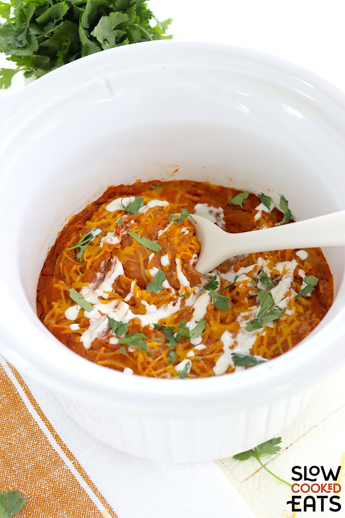 Slow cooker refried beans served in a white round crockpot and a white serving spoon.