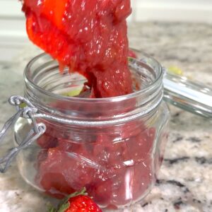 Transferring the slow cooker strawberry rhubarb jam to a clear lidded jar.