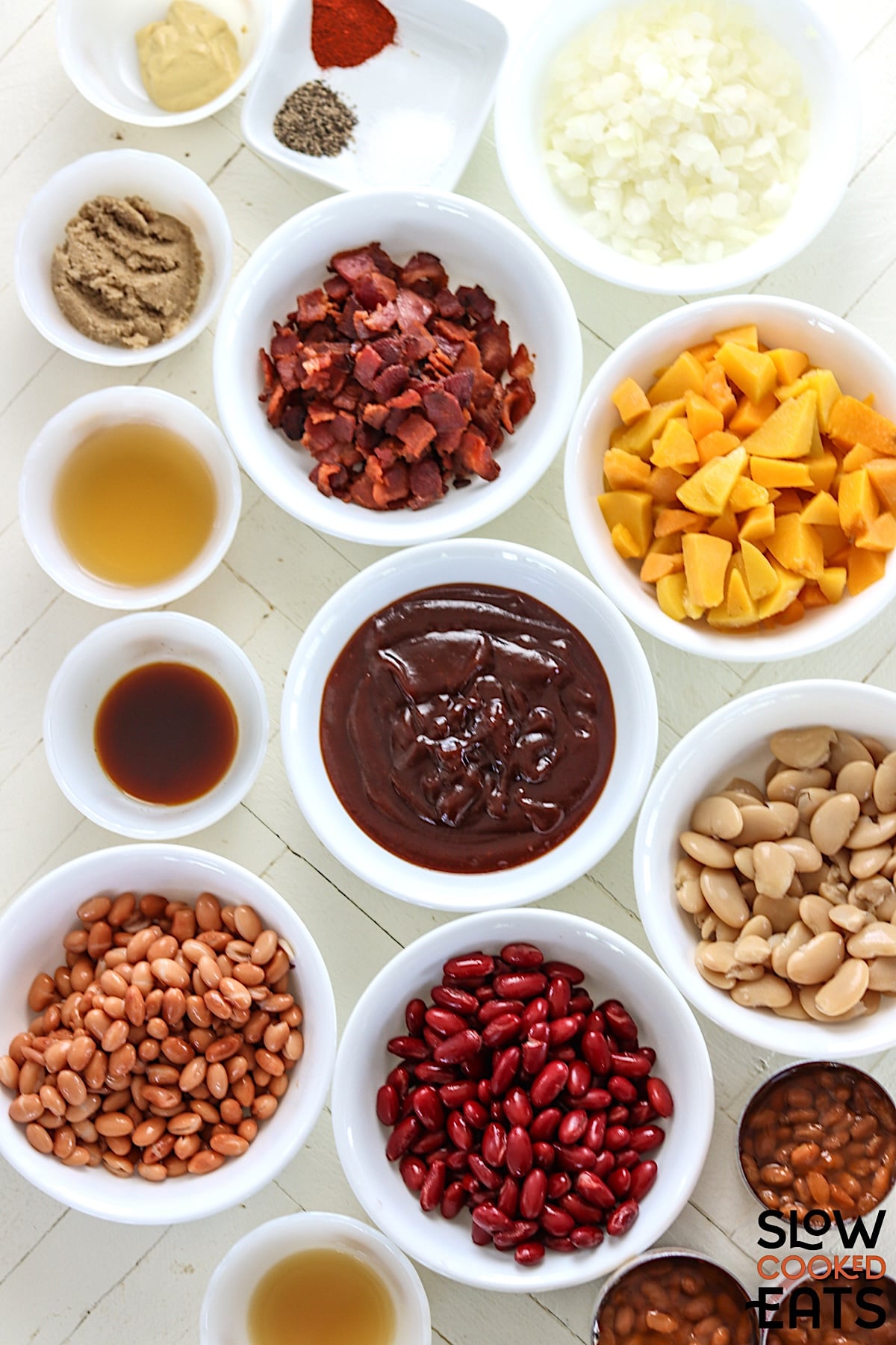 Ingredients needed for making peach bourbon baked beans crockot recipe on a white wooded board.
